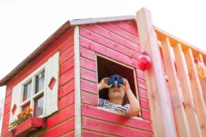 Photo of young boy looking out a playhouse window with binoculars