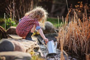 Photo of young girl filling a watering can in a backyard pond